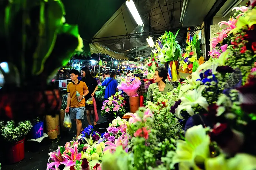 Shoppers walking among colourful flower stalls at Pak Khlong Talat in Bangkok